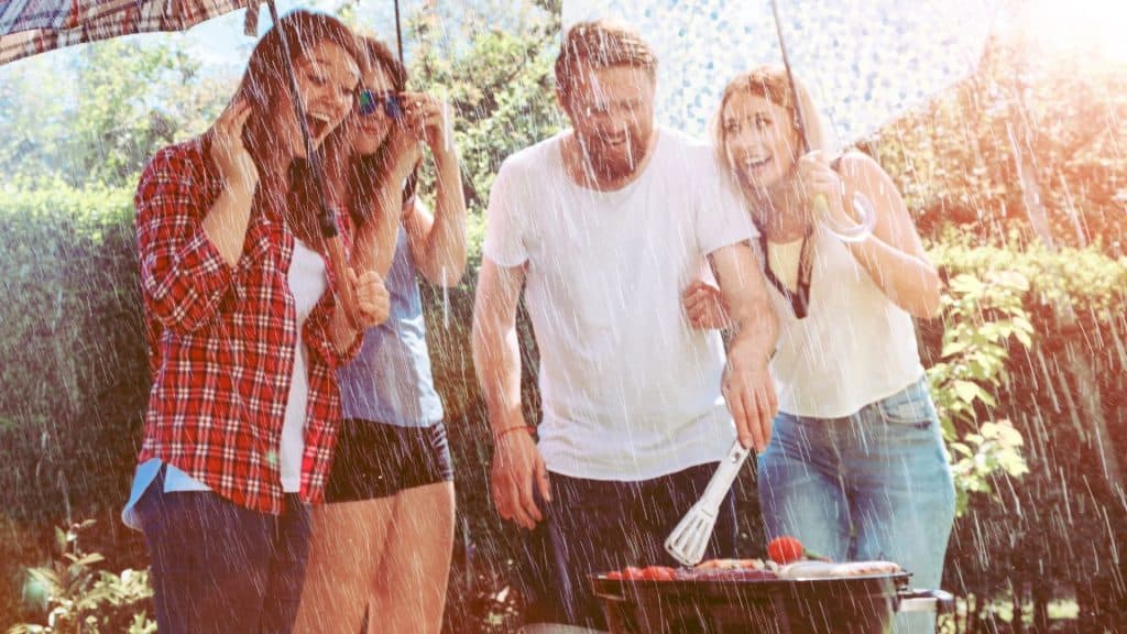 A group of friends laughing while grilling in the rain. 