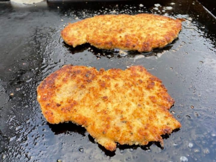 Golden brown breaded chicken cutlets frying on a Blackstone griddle. 