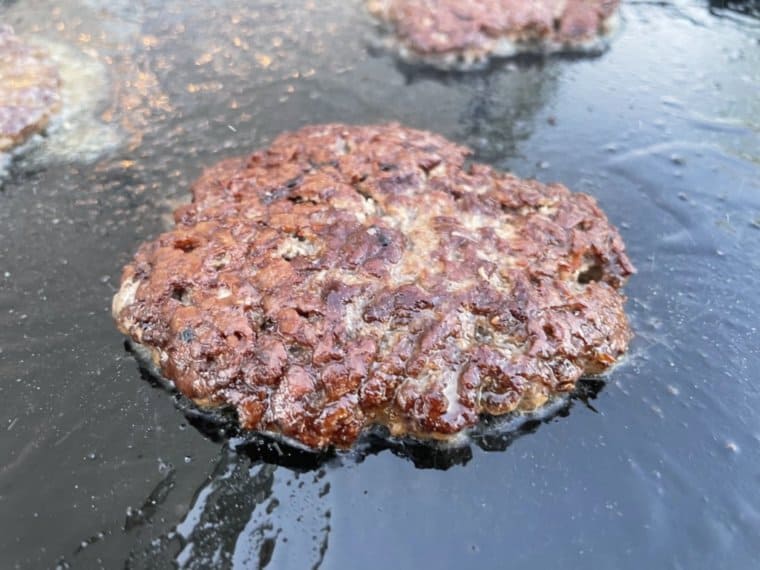A smash burger cooking on a griddle with a crispy and crunchy crust.