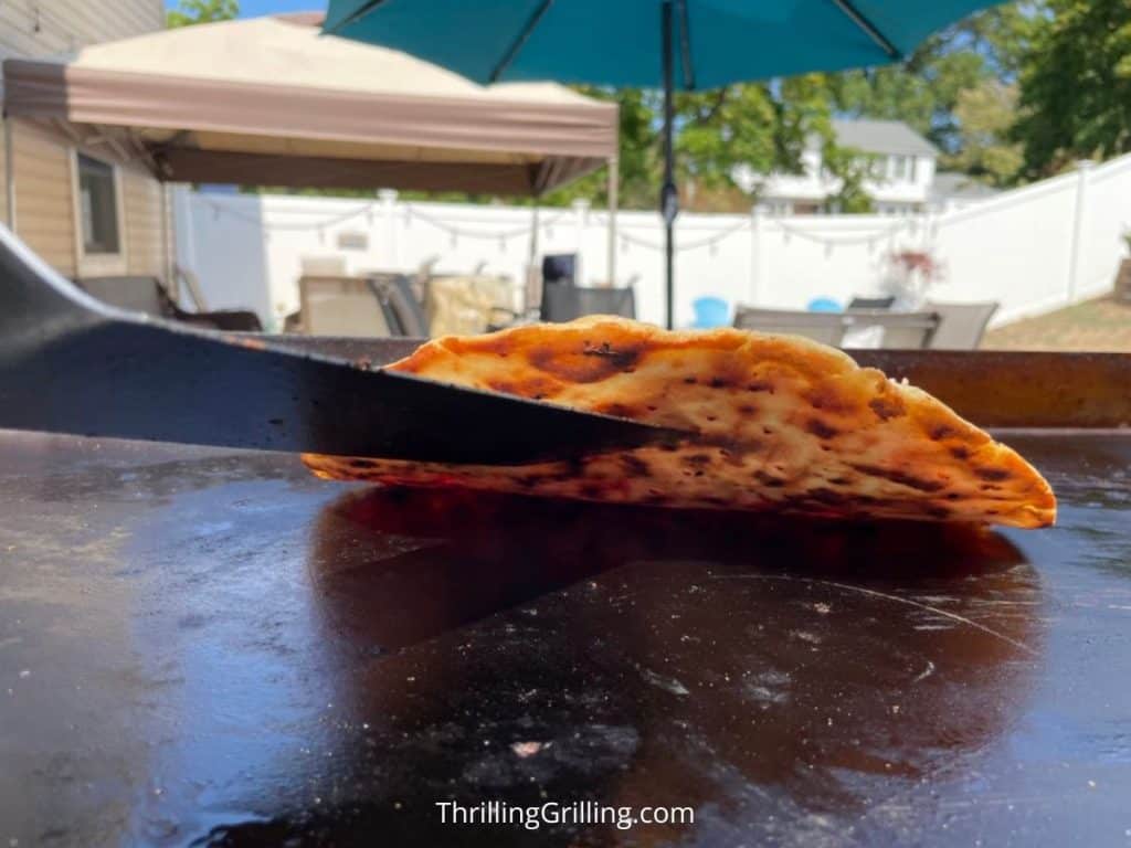 This crust pizza on blackstone with spatula holding it up to show the bottom being cooked.