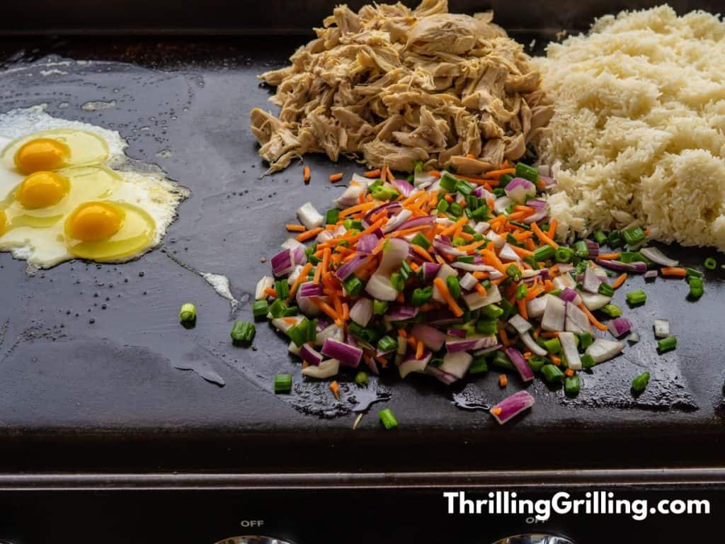 Eggs, chicken, rice, and veggies cooking on a griddle.