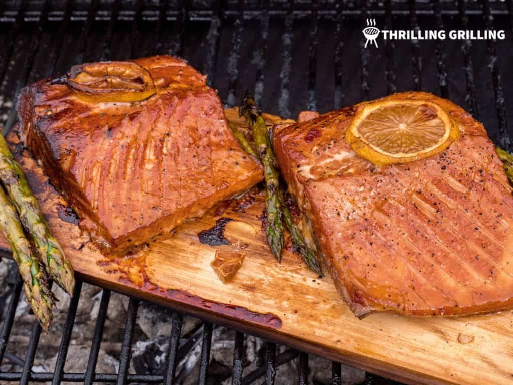 Two salmon filets and some asparagus cooking on a cedar plank
