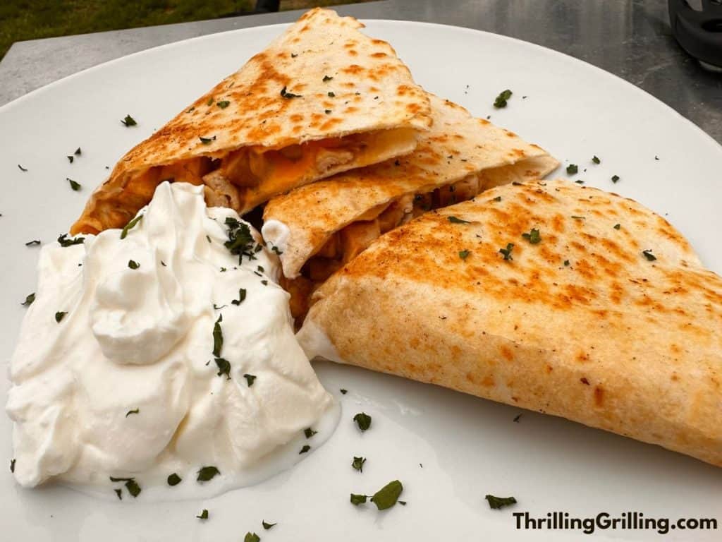 A plate of yummy Blackstone Chicken quesadillas with a side of sour cream.