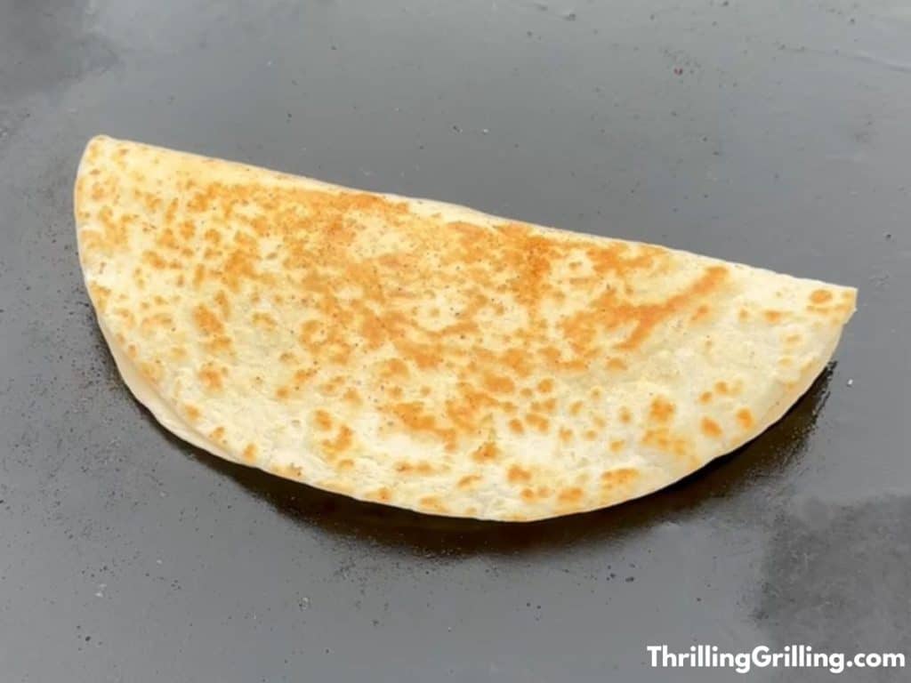 A golden brown quesadilla cooking on a Blackstone griddle