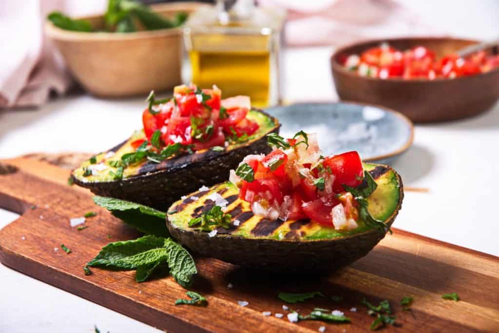 Two grilled avocado halves stuffed with pico de gallo sitting on a cutting board.