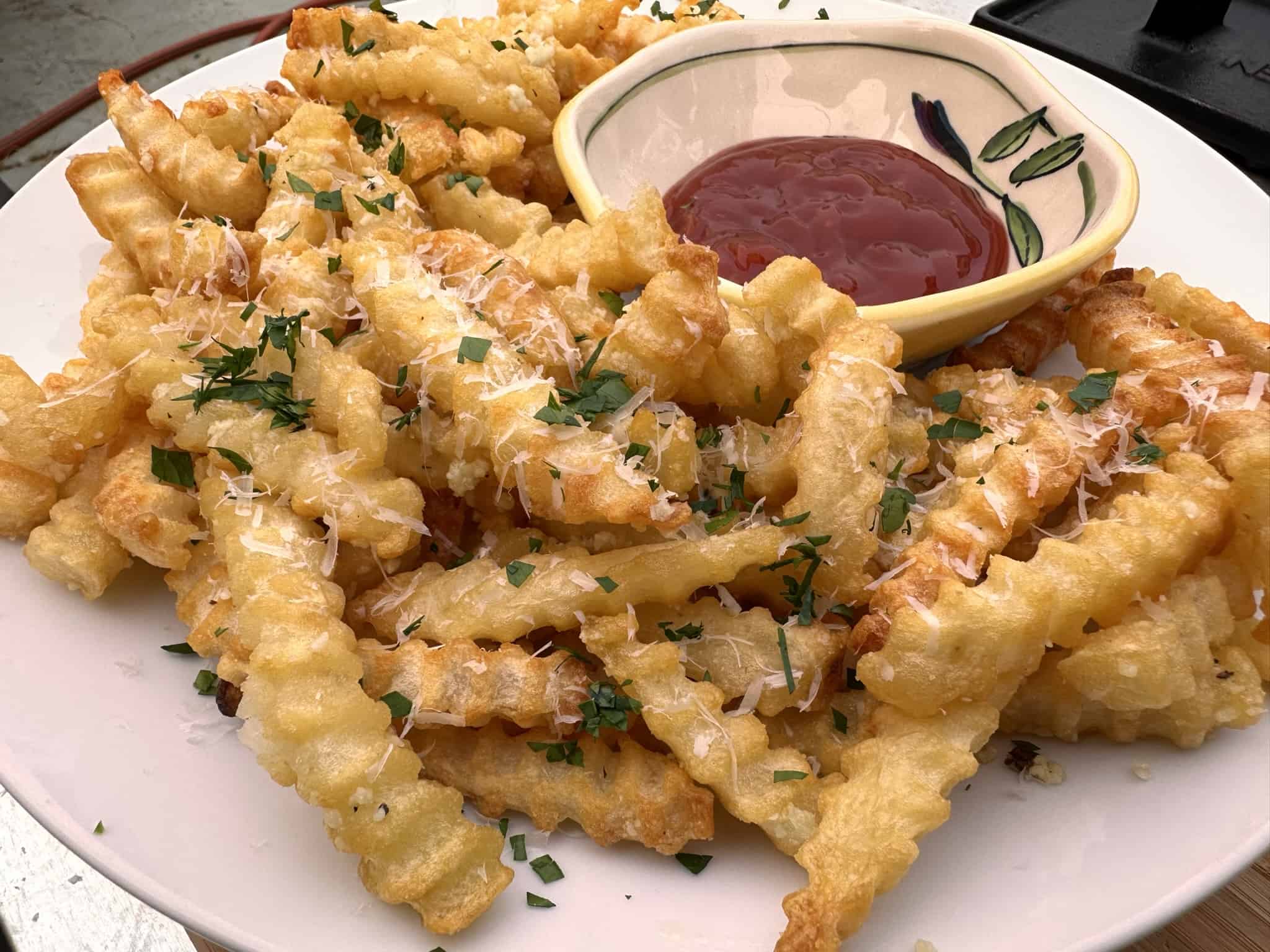 Garlic parmesan fries on a plate with a small dish of ketchup.
