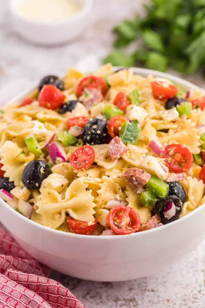 A white bowl with Italian pasta salad including farfalle pasta, cherry tomatoes, salami, scallions, and black olives.