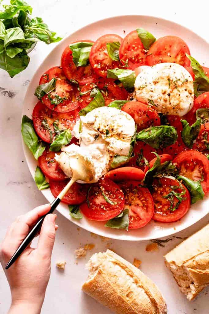 A white plate with freshly sliced tomatoes, creamy burrata cheese and garnished with basil.
