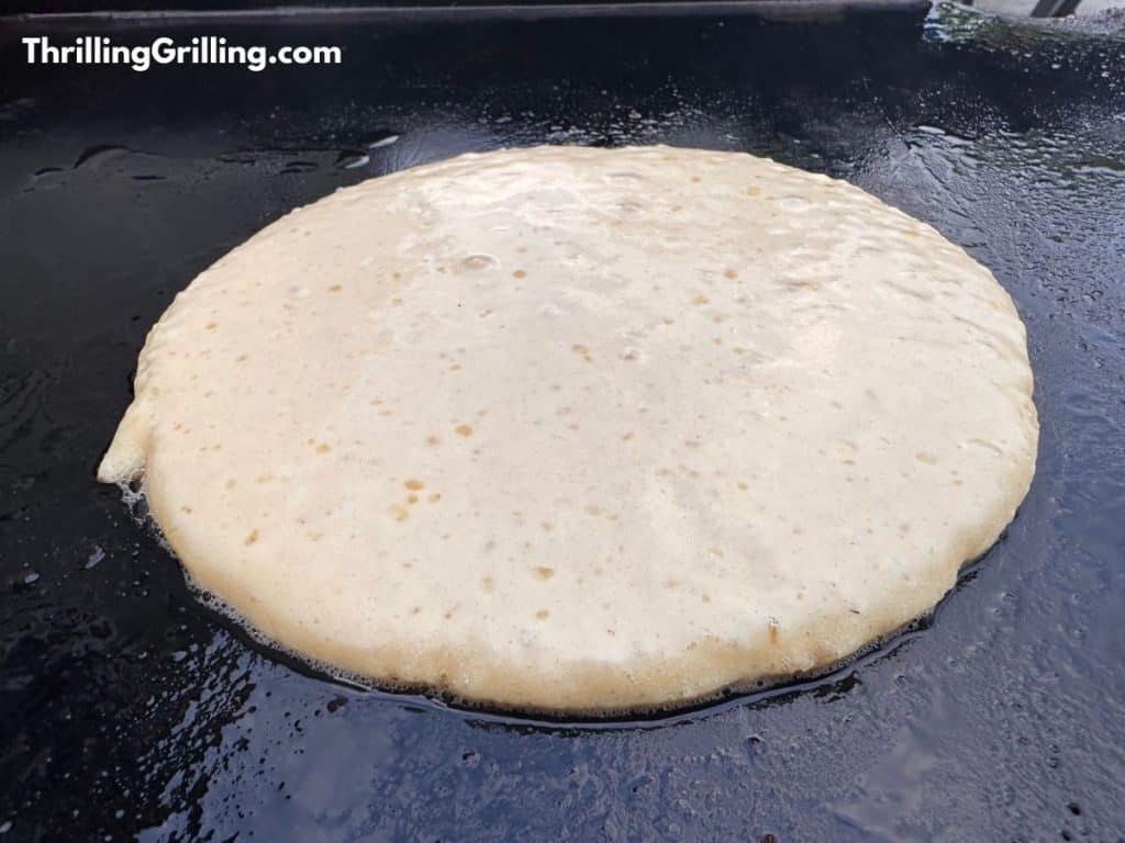 A pancake cooking on the griddle, just about ready to flip over. 