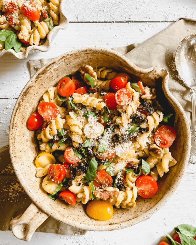 A rustic bowl full of pesto pasta salad with sundried tomatoes