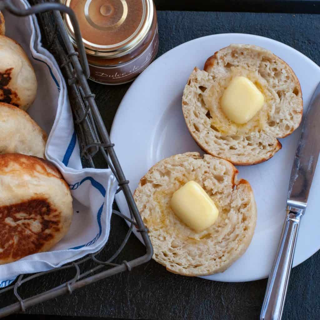 An English muffin on a plate with some melted butter. 