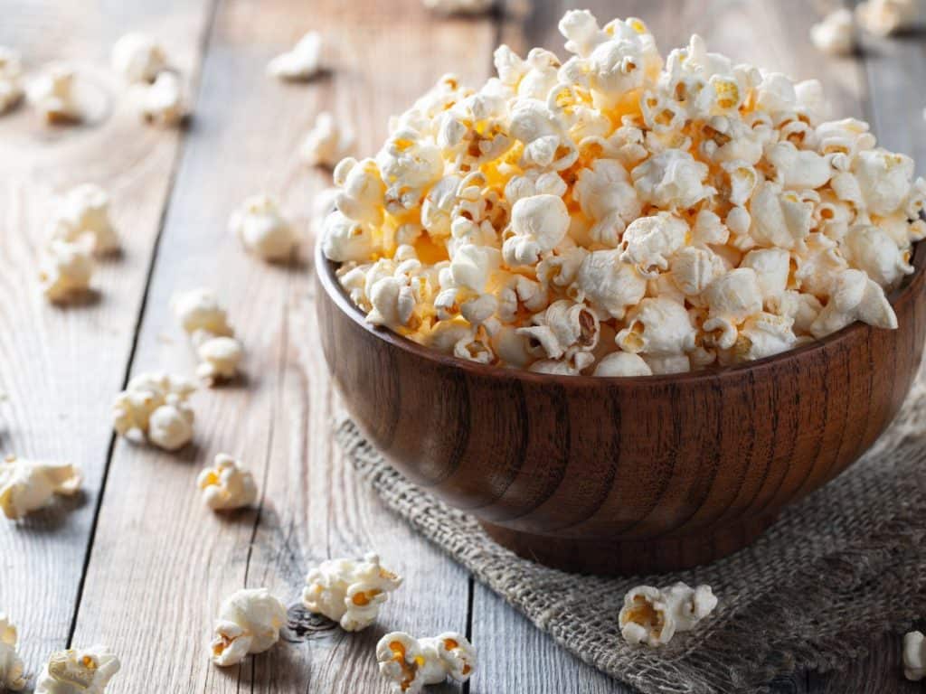 A wooden bowl overflowing with freshly popped popcorn.
