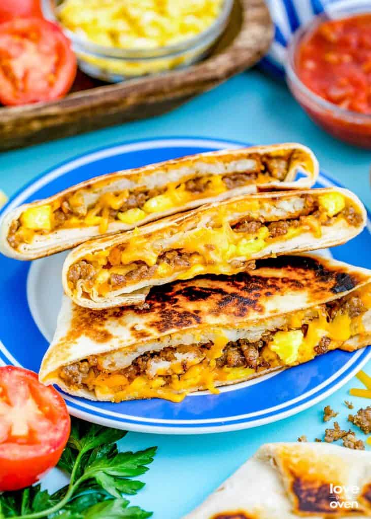 A plate with a breakfast crunchwrap sliced and oozing eggs, cheese, and ground sausage.