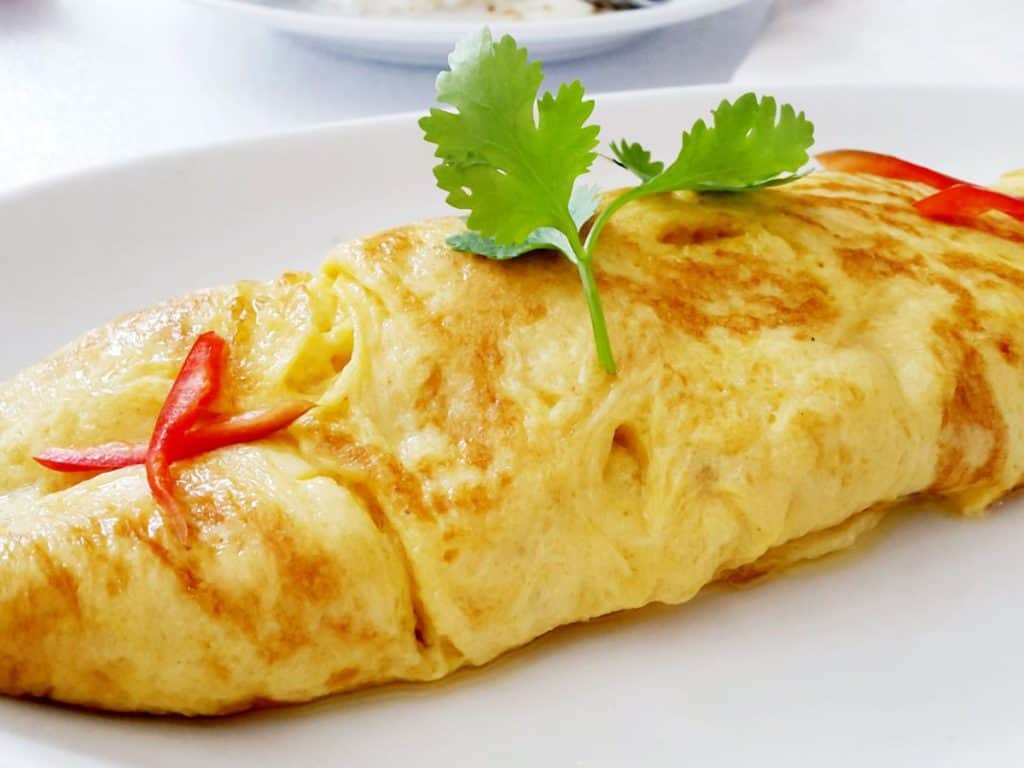 White plate with an omelet and garnished with parsley and red pepper slices.