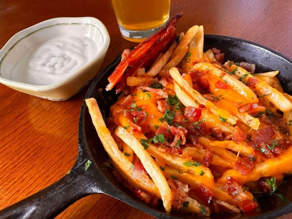 Small cast iron skillet loaded with cheese fries on a wooden kitchen table.