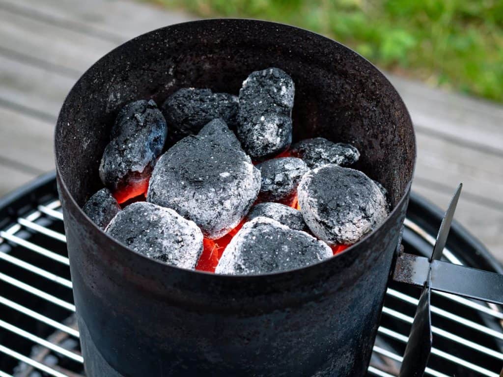 A charcoal chimney sitting on grill grates and full of coals that are mostly lit.