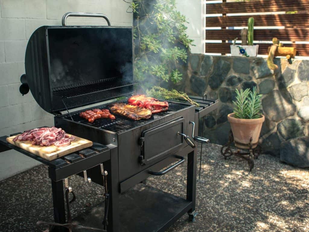 A lit grill with food cooking, demonstrating how far should grill be from house for safety reasons.
